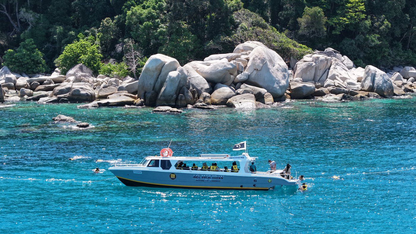 Bot AG Holiday di perairan pirus berhampiran batu granit Pulau Redang dengan peserta snorkeling di dalam air